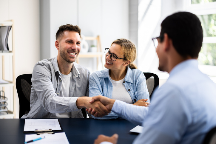 Young couple signing rental contract with real estate agent at apartment viewing, discussing financial plan and insurance with advisor.